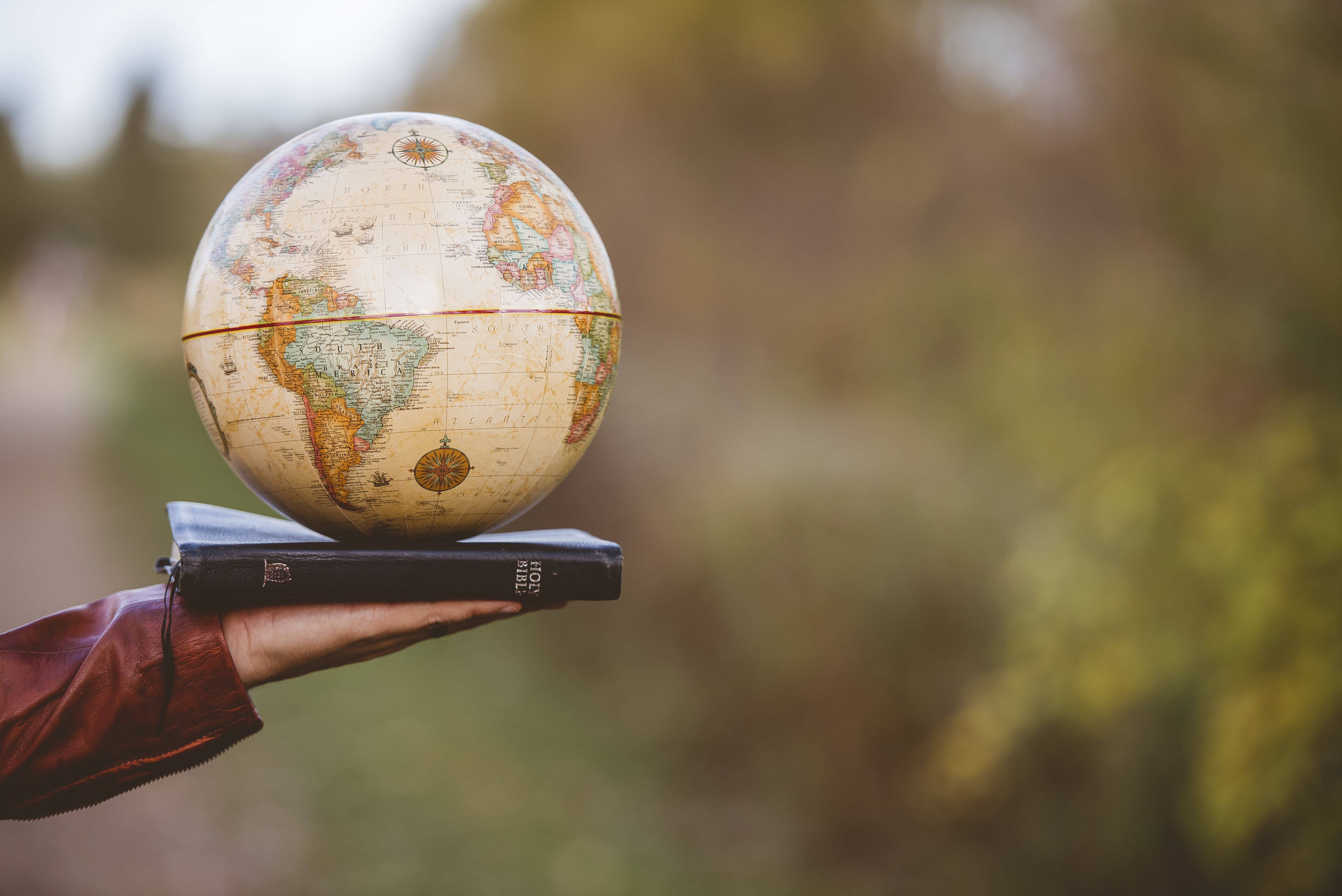 Closeup shot of a person holding bible with desk globe on top with a blurred background A closeup shot of a person holding bible with desk globe on top with a blurred background